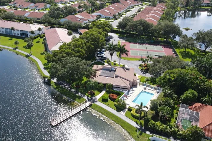 Aerial perspective of common area amenities including a swimming pool with paved deck, tennis courts, and a dock extending over the water