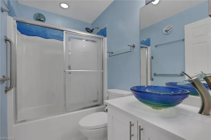 Bathroom featuring a white vanity cabinet with a solid surface countertop, blue glass vessel sink, chrome high-arc faucet, and a shower-tub combination with sliding glass doors