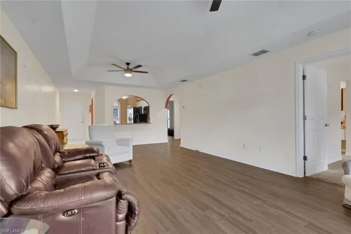 Tray ceiling with a central ceiling fan, wood-finish flooring, and arched architectural openings