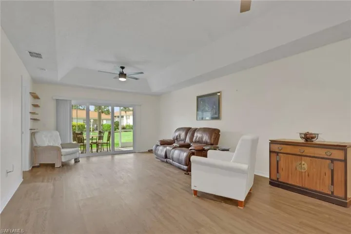 Tray ceiling featuring a central ceiling fan with an integrated light fixture, wood-finish flooring, and sliding glass doors with vertical blinds