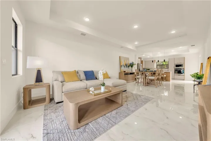Living room featuring a raised ceiling, light marble finish flooring, and recessed lighting