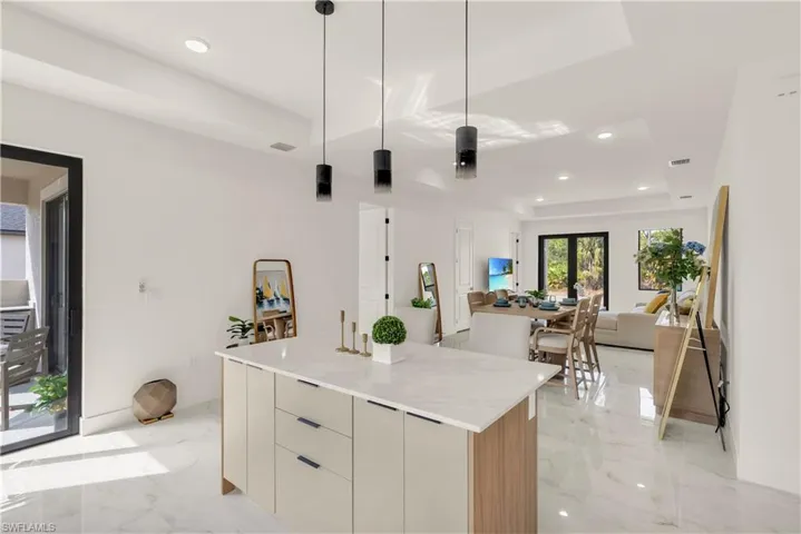 Kitchen featuring modern cabinets, hanging light fixtures, recessed lighting, a raised ceiling, and light marble finish floors