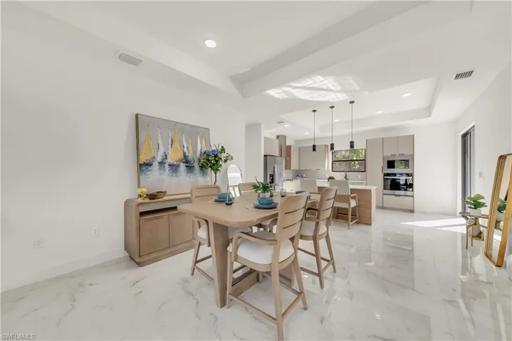 Dining space with light marble finish flooring, a raised ceiling, and recessed lighting