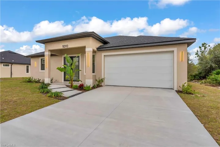 Prairie-style home featuring a front lawn, stucco siding, concrete driveway, an attached garage, and roof with shingles