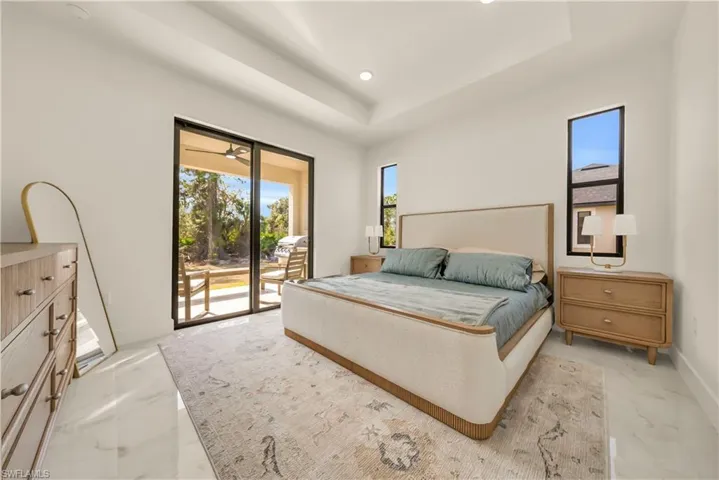 Bedroom with a tray ceiling, access to outside, light marble finish floors, and recessed lighting