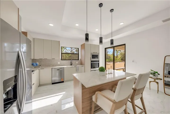 Kitchen featuring appliances with stainless steel finishes, pendant lighting, a kitchen breakfast bar, light stone countertops, and modern cabinets