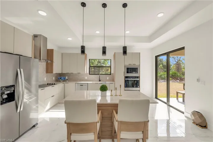 Kitchen featuring appliances with stainless steel finishes, hanging light fixtures, light marble finish flooring, a kitchen breakfast bar, and modern cabinets