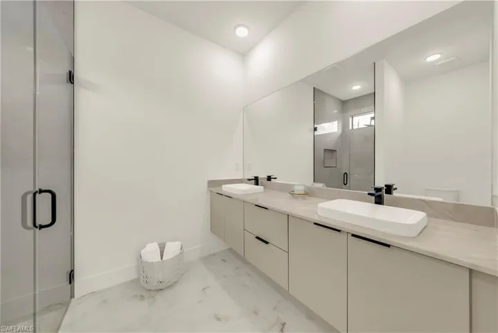 Bathroom featuring double vanity, a shower stall, and light marble finish flooring