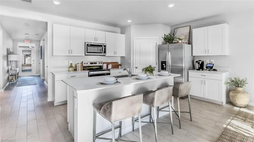 Model home. Kitchen featuring stainless steel appliances, a kitchen bar, white cabinetry, wood tiled floors, and a center island with sink