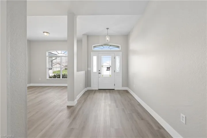 Wood-finish flooring, white trim, and a white front entry door with a transom window and sidelights