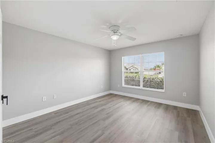 Light gray painted walls, wood-finish flooring, white ceiling fan with integrated lighting, and a white-framed window