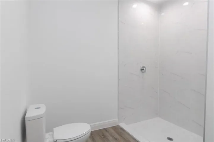 Master bathroom featuring tiled shower, toilet, and vinyl floors