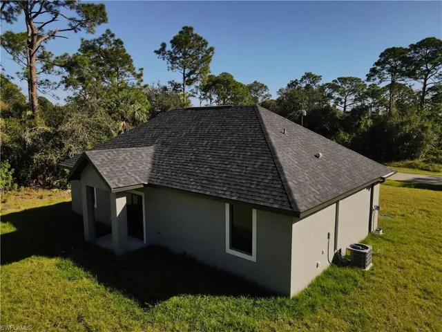 View of side of property featuring a shingled roof, central air condition unit, a yard, and stucco siding