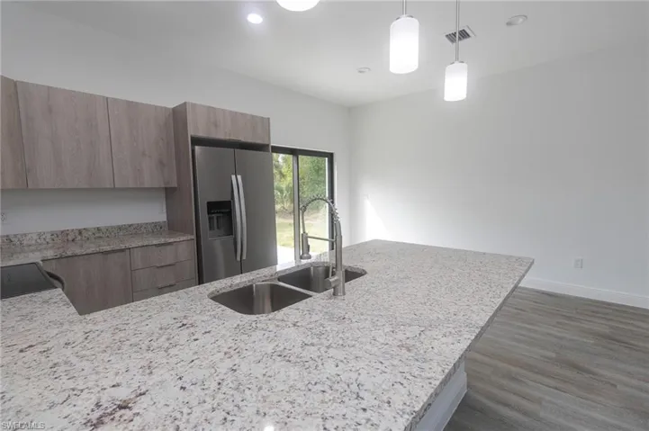 Kitchen featuring a sink, stainless steel fridge with ice dispenser, light stone countertops, vinyl style floors, and modern cabinets