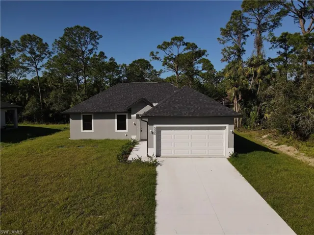 Ranch-style home with concrete driveway, a front yard, roof with shingles, stucco siding, and a garage