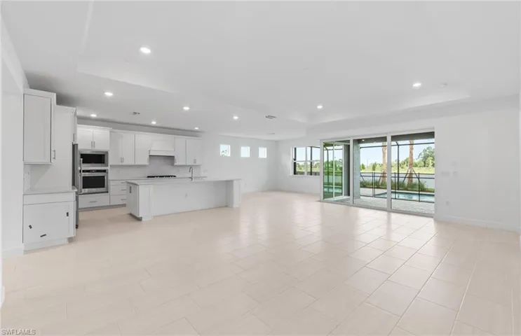 Kitchen featuring tasteful backsplash, stainless steel microwave, custom exhaust hood, an island with sink, and a raised ceiling