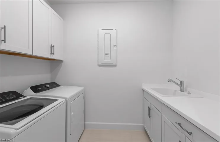 Clothes washing area with washing machine and clothes dryer, sink, cabinets, and light tile patterned floors