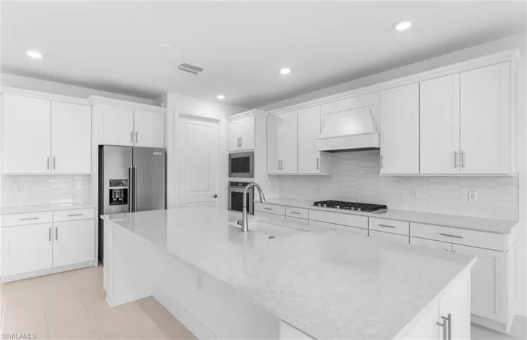 Kitchen with appliances with stainless steel finishes, custom range hood, tasteful backsplash, and a center island with sink
