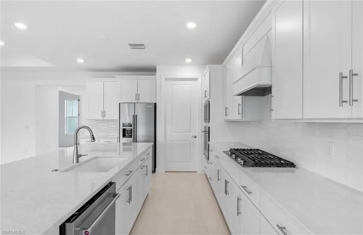 Kitchen featuring white cabinetry, custom exhaust hood, tasteful backsplash, stainless steel appliances, and sink