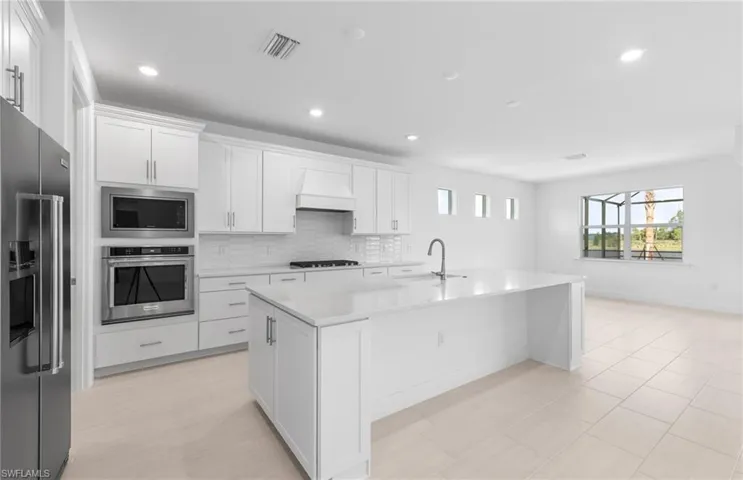 Kitchen with custom range hood, white cabinets, backsplash, a kitchen island with sink, and stainless steel appliances