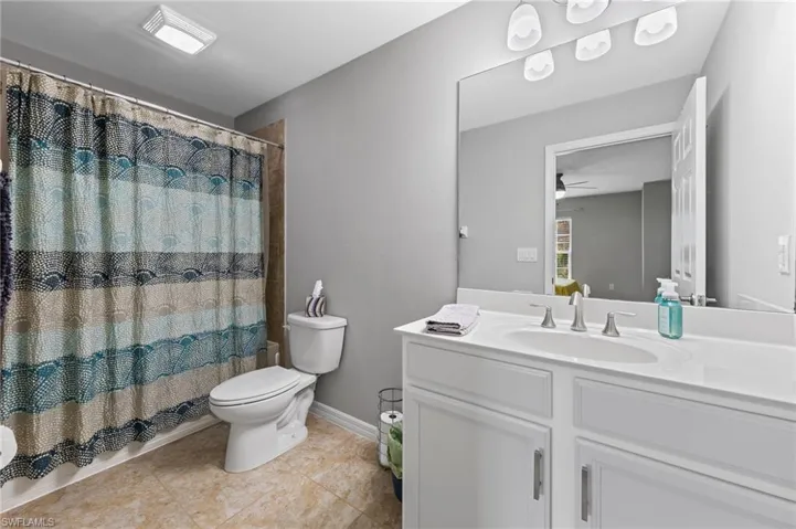 Full bathroom with vanity, a shower with shower curtain, light tile patterned floors, and ceiling fan