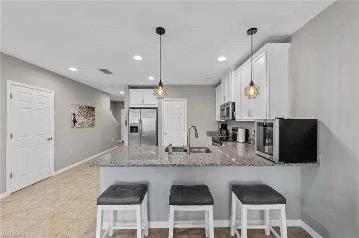 Kitchen featuring a peninsula, appliances with stainless steel finishes, white cabinets, recessed lighting, and a kitchen bar