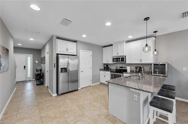 Kitchen featuring appliances with stainless steel finishes, white cabinets, dark stone countertops, a peninsula, and a kitchen breakfast bar