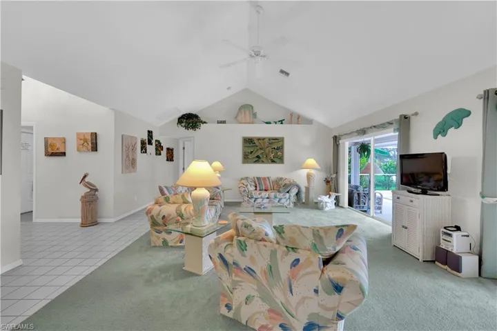 Carpeted living area with ceiling fan, high vaulted ceiling, and tile patterned flooring