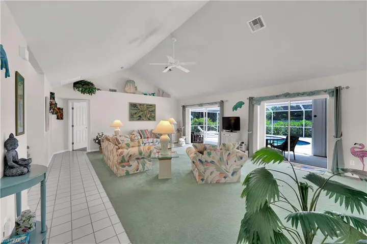 Living area with carpet floors, tile patterned flooring, high vaulted ceiling, and a ceiling fan