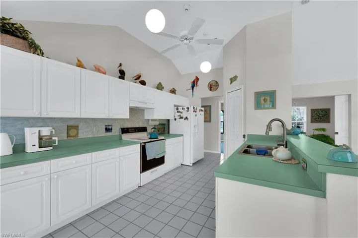 Kitchen featuring white appliances, white cabinets, ceiling fan, tasteful backsplash, and high vaulted ceiling
