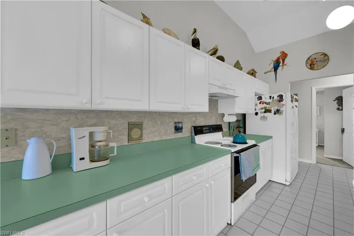 Kitchen featuring white appliances, white cabinets, backsplash, under cabinet range hood, and light tile patterned flooring
