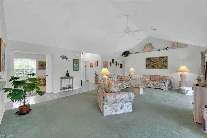 Tiled living area with a ceiling fan, carpet flooring, and high vaulted ceiling