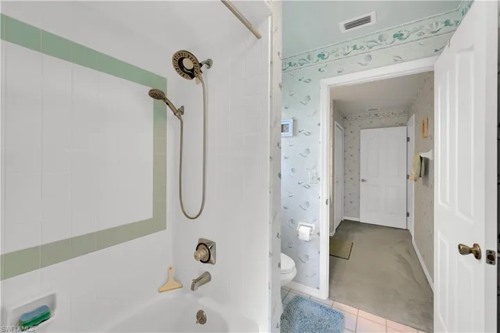 Full bathroom with wallpapered walls, tile patterned flooring, shower / bath combination, and carpet