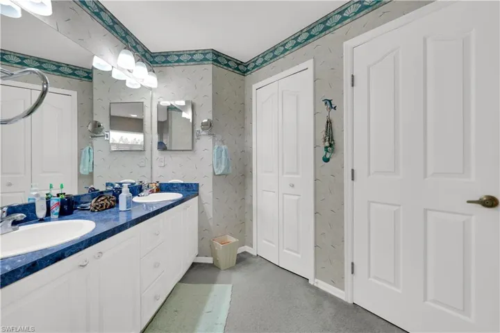 Full bathroom with double vanity, wallpapered walls, and light carpet