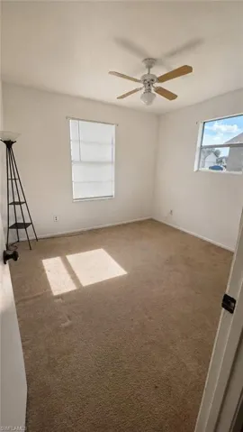 Carpeted interior space with a ceiling fan and light fixture, featuring two windows with horizontal blinds