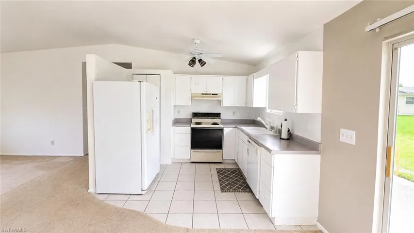Open-concept kitchen featuring white cabinetry, a white refrigerator, and a black range
