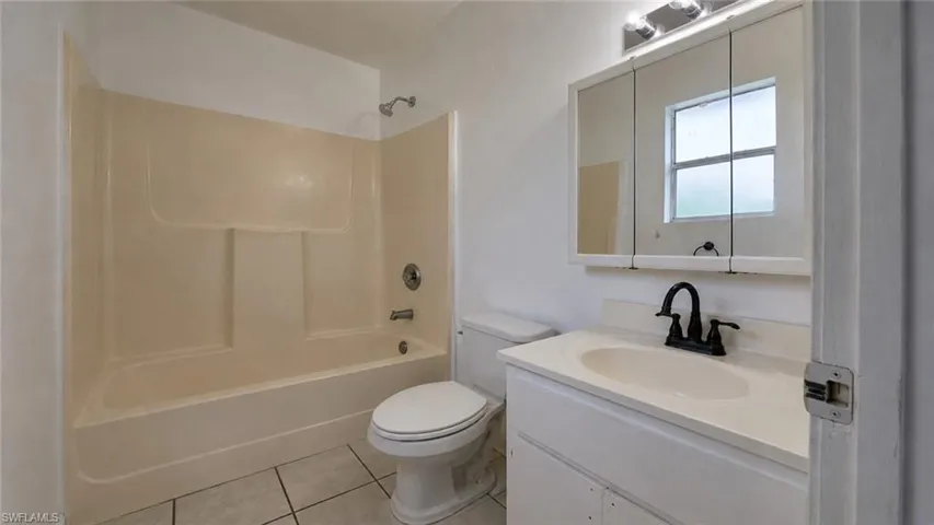 Bathroom featuring a shower-tub combination, a vanity with an integrated sink, a dark-finish faucet, a mirrored medicine cabinet, and a window