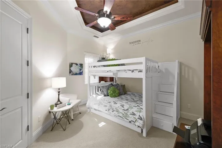 Bedroom featuring a lighted tray ceiling, ceiling fan, carpet flooring, and crown molding