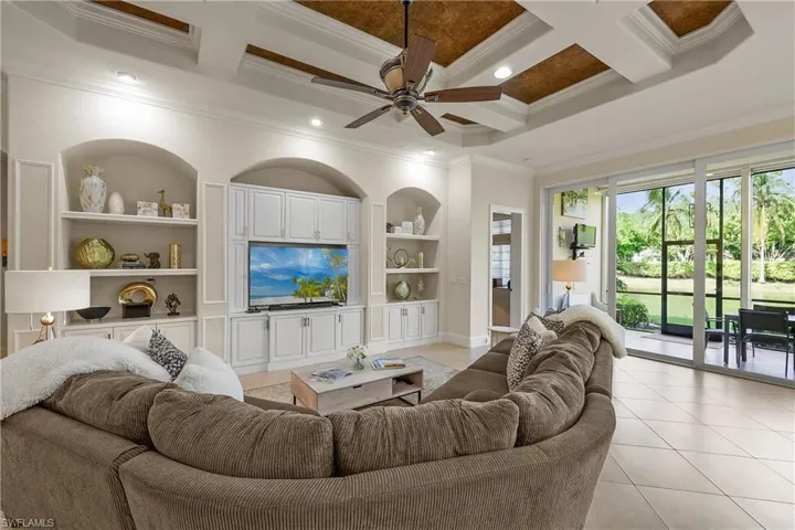 Living room with coffered ceiling, built in shelves, ceiling fan, ornamental molding, and beamed ceiling