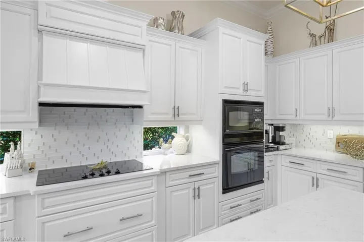 Kitchen featuring black appliances, decorative backsplash, white cabinets, and custom range hood