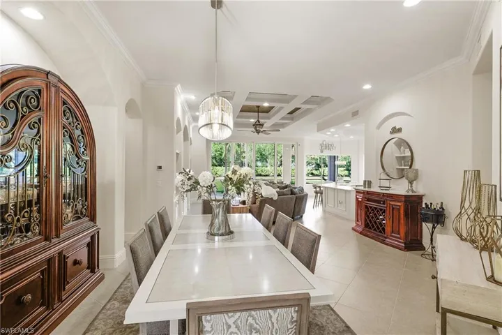 Tiled dining area with beam ceiling, ceiling fan with notable chandelier, coffered ceiling, and ornamental molding