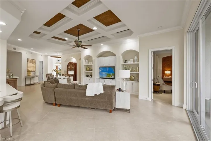 Living room featuring coffered ceiling, built in shelves, ceiling fan, crown molding, and beamed ceiling
