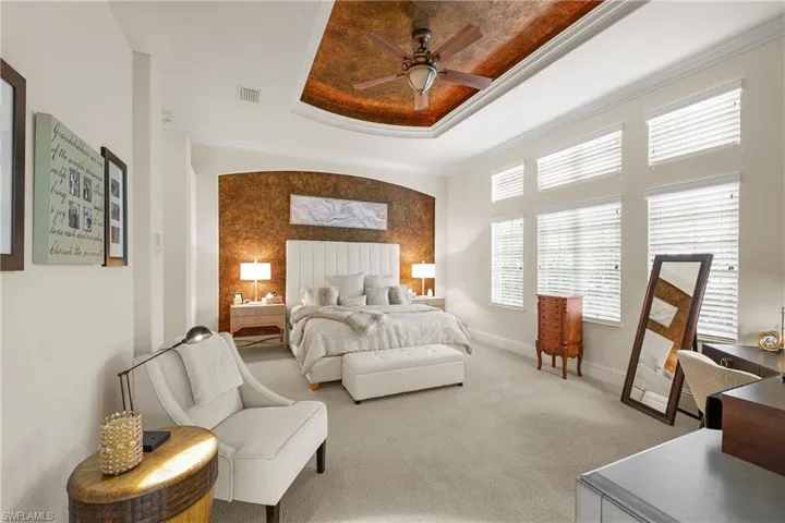 Carpeted bedroom featuring ceiling fan, a lighted tray ceiling, and ornamental molding