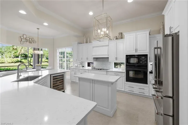 Kitchen featuring pendant lighting, black appliances, a large island, white cabinetry, and beverage cooler