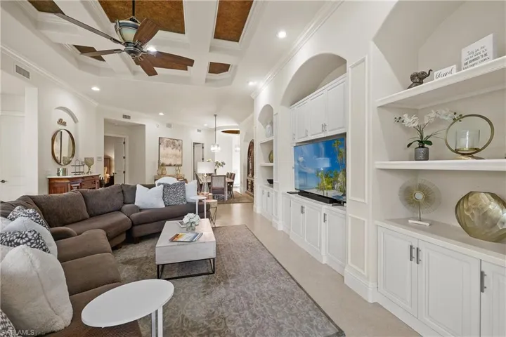 Living room with beam ceiling, ornamental molding, coffered ceiling, and ceiling fan