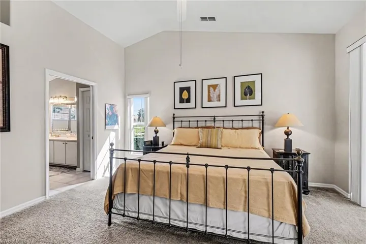 Bedroom featuring light colored carpet, lofted ceiling, and ensuite bath