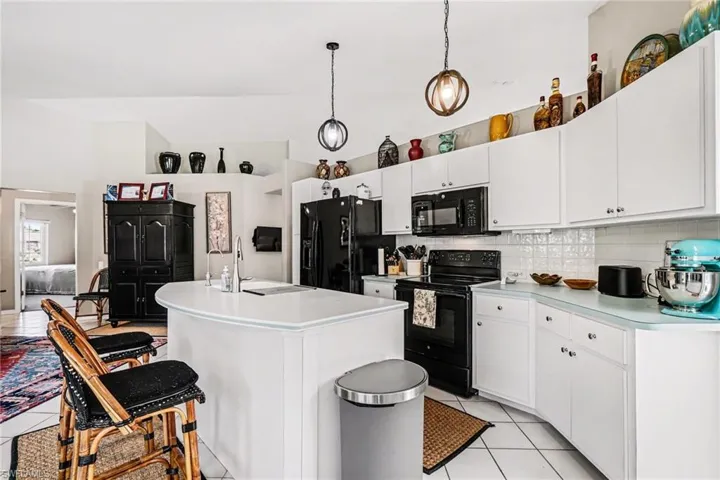 Kitchen featuring black appliances, light countertops, decorative backsplash, white cabinets, and decorative light fixtures