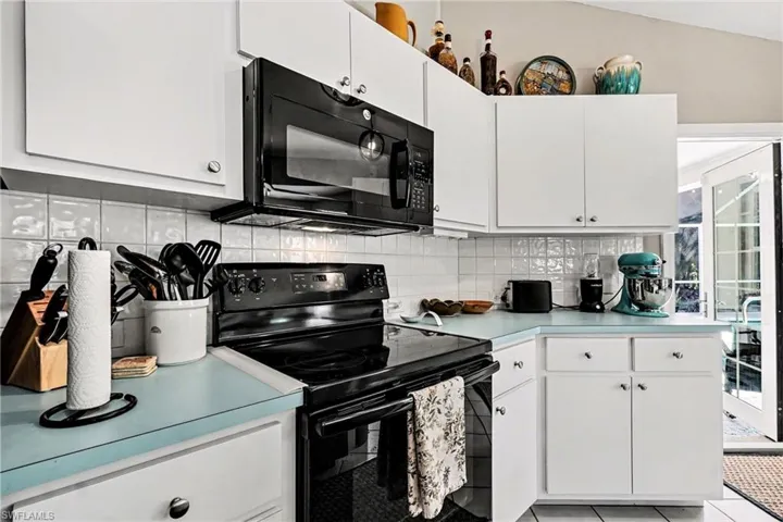 Kitchen with black appliances, light countertops, white cabinets, and light tile patterned flooring