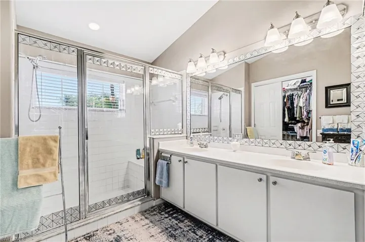 Bathroom featuring double vanity, a stall shower, a walk in closet, and light tile patterned flooring