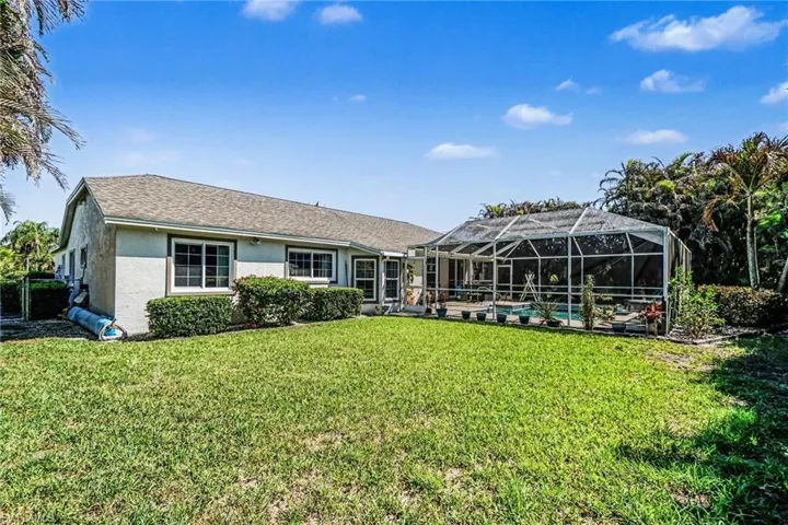 Rear view of property featuring an outdoor pool, stucco siding, a sunroom, and a lawn